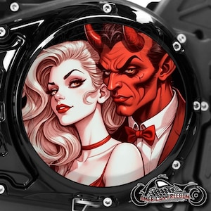 Puede incluir: Cubierta de motor de motocicleta negra con un gráfico circular que presenta un diablo rojo y una mujer con cabello rubio. El diablo viste un traje y una pajarita. La mujer lleva un vestido rojo y una gargantilla. Las palabras "AMERICAN FREEDOM" están en la parte inferior.