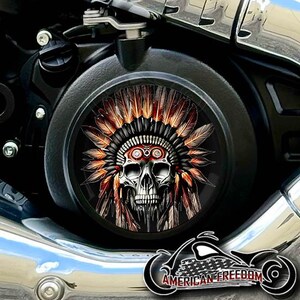Op de afbeelding: Zwarte motorfietsmotordeksel met een schedelontwerp met een Indiaanse hoofdtooi met oranje en bruine veren. Het logo "AMERICAN FREEDOM" is zichtbaar.