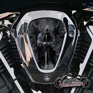 Könnte beinhalten: Ein schwarzer und silberner Motorrad-Lufteinlassdeckel mit einer Grafik einer Kapuzenfigur mit Flügeln, die ein Schwert hält.