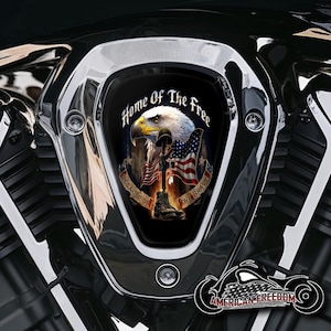 Könnte beinhalten: Ein Motorradteil mit Chromoberfläche, das ein zentrales Emblem mit einem Adler, der amerikanischen Flagge und dem Text "Home Of The Free Because Of The Brave" zeigt. Das Emblem ist von einem Chromrahmen umgeben.