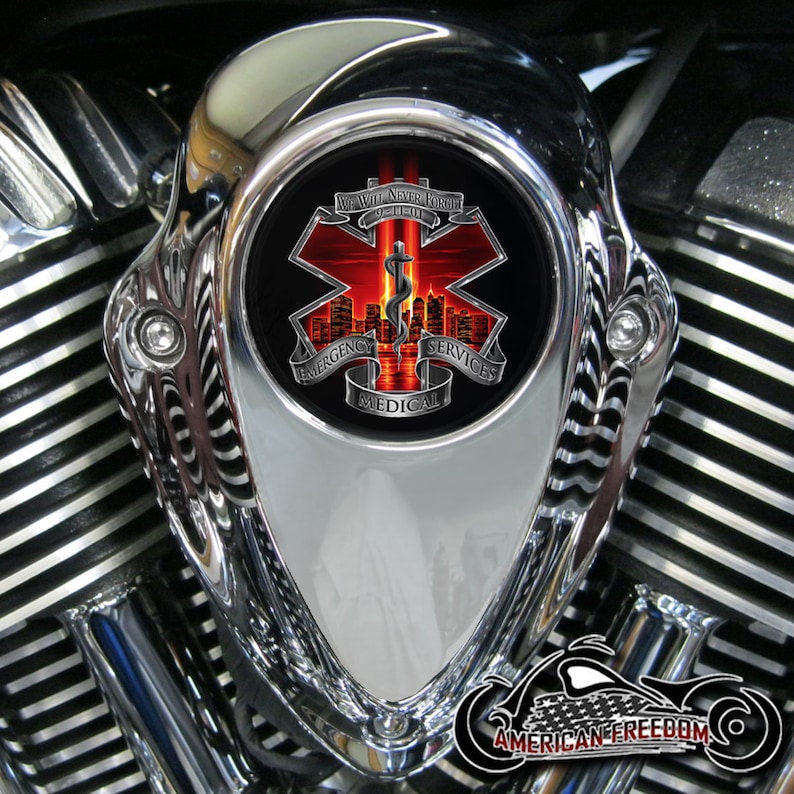 Puede incluir: Una cubierta de filtro de aire de motocicleta cromada con un s&iacute;mbolo m&eacute;dico rojo, blanco y azul con el texto "We Will Never Forget 9-11-01" y "Emergency Medical Services".