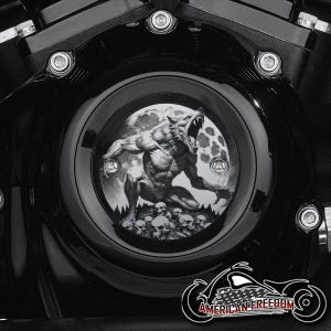 Puede incluir: Cubierta negra del motor de una motocicleta con un gráfico circular que representa un hombre lobo aullando a la luna, con calaveras en la base. La cubierta está rodeada de pernos y el logotipo American Freedom.