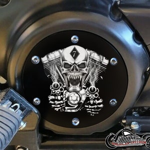 Puede incluir: Tapa de motor de motocicleta negra con un diseño de calavera y huesos cruzados. La calavera lleva un diamante con el número 7 en su interior. La tapa está hecha de metal y tiene un acabado negro.