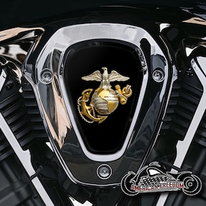 Könnte beinhalten: Nahaufnahme einer Motorrad-Motorabdeckung mit Chrom-Finish. Sie zeigt ein goldenes Emblem eines Adlers auf einer Weltkugel und einem Anker, dem Symbol des US Marine Corps. Die Worte "AMERICAN FREEDOM" sind unten rechts in einer Motorradgrafik zu sehen.