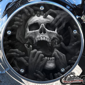 Könnte beinhalten: Eine schwarz-weiße Motorradabdeckung mit einem Totenkopf- und Handdesign. Der Totenkopf ist von Händen umgeben, die nach ihm greifen. Die Abdeckung ist rund und hat einen verchromten Rand.