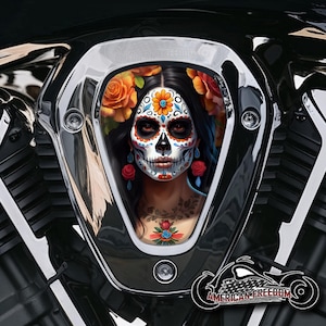 Könnte beinhalten: Ein schwarzer und verchromter Motorrad-Luftfilterdeckel mit einem farbenfrohen Totenkopf-Design im Stil des Día de Muertos. Der Schädel hat ein weißes Gesicht mit schwarzen Augen, einer roten Nase und einem bunten Blumenmuster.