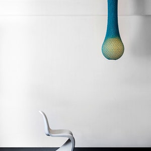 May include: A white modern chair with a curved back and seat sits in front of a white wall. A teal and yellow hanging light fixture hangs from the ceiling.