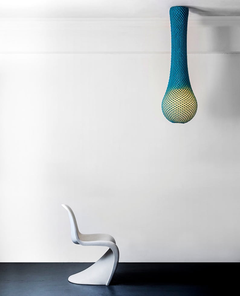 May include: A white modern chair with a curved back and seat sits in front of a white wall. A teal and yellow hanging light fixture hangs from the ceiling.
