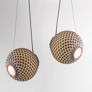 May include: Two woven sphere pendant lights with a black cord hanging from the ceiling. The spheres are made of a light brown material and have a white interior.