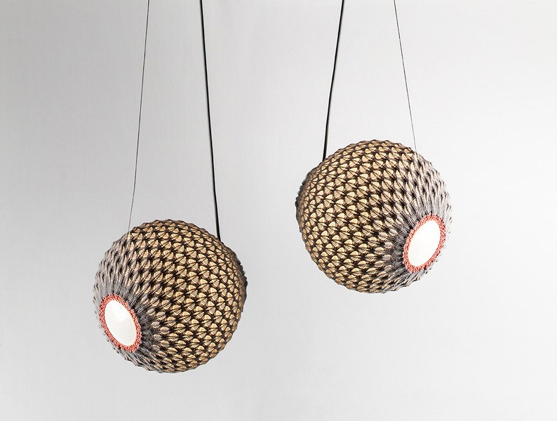 May include: Two woven sphere pendant lights with a black cord hanging from the ceiling. The spheres are made of a light brown material and have a white interior.