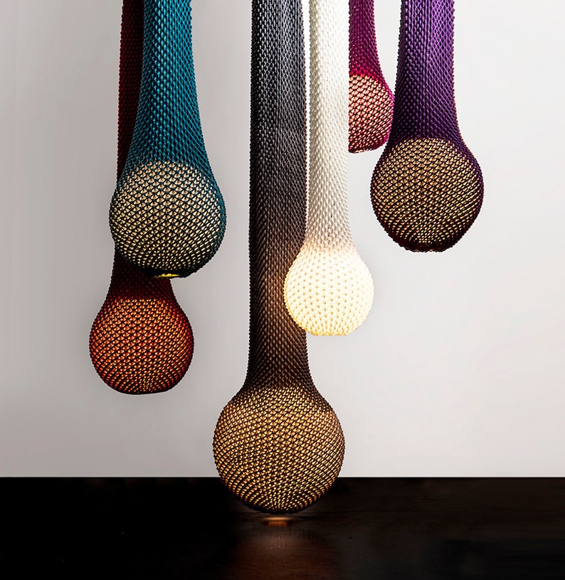 May include: Six hanging light fixtures made of woven mesh in various colors, including teal, gray, white, pink, and purple. The lights are shaped like teardrops and emit a warm glow.