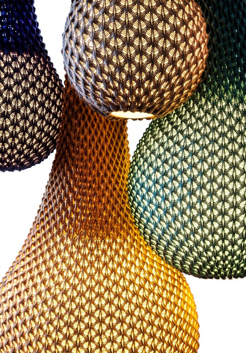 May include: Four hanging light fixtures made of woven material in blue, brown, green, and grey colours. The light fixtures are round and have a textured surface.