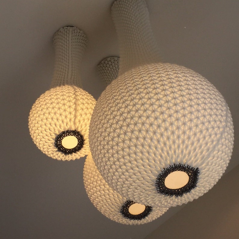May include: Three white, round, woven pendant lights with black accents. The lights are hanging from the ceiling and are illuminated.