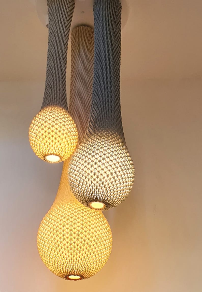 May include: Three hanging light fixtures with a woven, net-like design. The fixtures are shaped like teardrops and are illuminated with warm, yellow light.