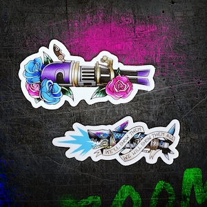 May include: Two stickers on a dark background. The top sticker features a purple and gold gun design with blue and pink roses. The bottom sticker is a shark with a mechanical design, with the text "WE'LL SHOW THEM, WE WILL SHOW THEM ALL".