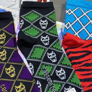 Puede incluir: Cuatro pares de calcetines coloridos con un patrón de diamante y un gráfico de calavera. Los calcetines son negros con patrones verdes, morados, azules y rojos.