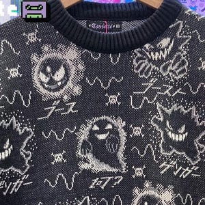 Puede incluir: Suéter negro de punto con cuello redondo y mangas largas. El suéter presenta un patrón repetido de personajes de fantasmas de dibujos animados blancos y texto japonés. La marca "cassette" es visible en la parte superior de la espalda del suéter.