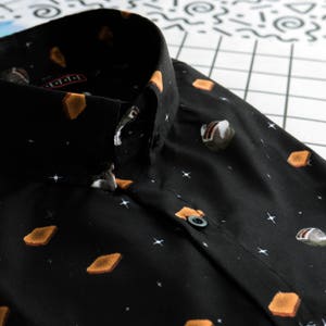 Könnte beinhalten: Ein schwarzes Hemd mit Knöpfen und einem sich wiederholenden Muster aus Toast und einem Retro-Toaster. Das Hemd hat einen weißen Kragen und einen Knopfverschluss.