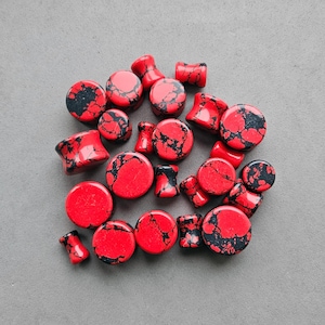 May include: A collection of red and black marbled ear gauges. The gauges are made of a smooth, polished stone and have a variety of sizes.