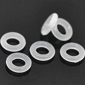 May include: A collection of six translucent white rubber O-rings. The O-rings are circular with a hole in the center. They are arranged on a dark surface, with some overlapping.