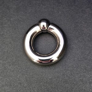 Könnte beinhalten: Ein silberner Metallring mit einer Kugel auf einer Seite. Der Ring ist glatt und glänzend.