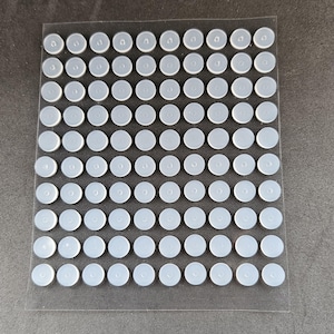May include: A sheet of clear adhesive-backed round dots, arranged in a grid pattern. The dots are white and opaque.