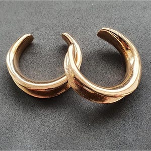 May include: A pair of gold-toned hoop earrings with a twisted design. The earrings are made of metal and have a smooth finish.