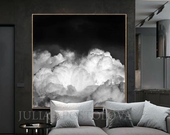 May include: Black and white cloudscape art print. The artwork features a dramatic depiction of billowing clouds against a dark sky. The print is framed in a gold-colored frame and hangs above a gray sofa in a modern living room.