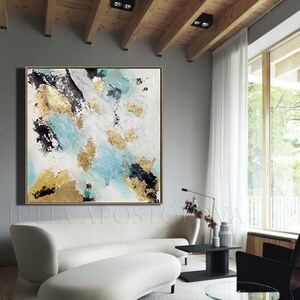 May include: Abstract painting with gold leaf accents on a white canvas. The painting features shades of blue, black, and white. The painting is hanging on a gray wall in a modern living room.