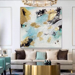 May include: Abstract painting with blue, white, and gold accents. The painting features a modern, abstract design with splashes of color and gold leaf. The painting is framed and hanging on a white wall above a couch.