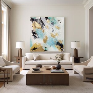 A modern living room featuring a large abstract painting with turquoise, gold, black, and white colors on the wall. The room has a light-colored sofa with beige cushions, two matching armchairs, table lamps, and a wooden coffee table in the center.