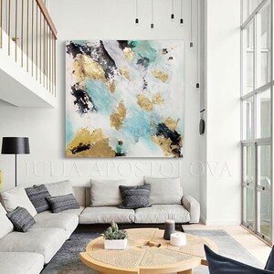 May include: Abstract painting with gold, black, and teal accents on a white canvas. The painting is hanging on a white wall in a modern living room with a white couch, a coffee table, and a black chair.