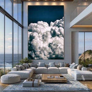 May include: A large, abstract painting of white clouds against a dark blue sky. The painting is hanging on a wall in a modern living room with a large sectional sofa and a coffee table.