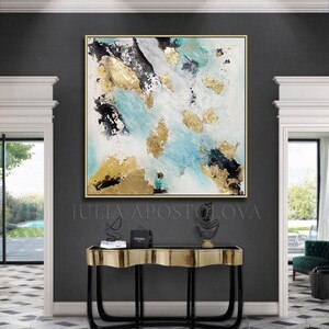 May include: Abstract painting with gold, black, and blue accents on a white background. The painting is framed in gold and hangs above a black and gold console table with a black and gold sculpture on top. The text "JULIA APOSTOLOVA" is visible below the painting.