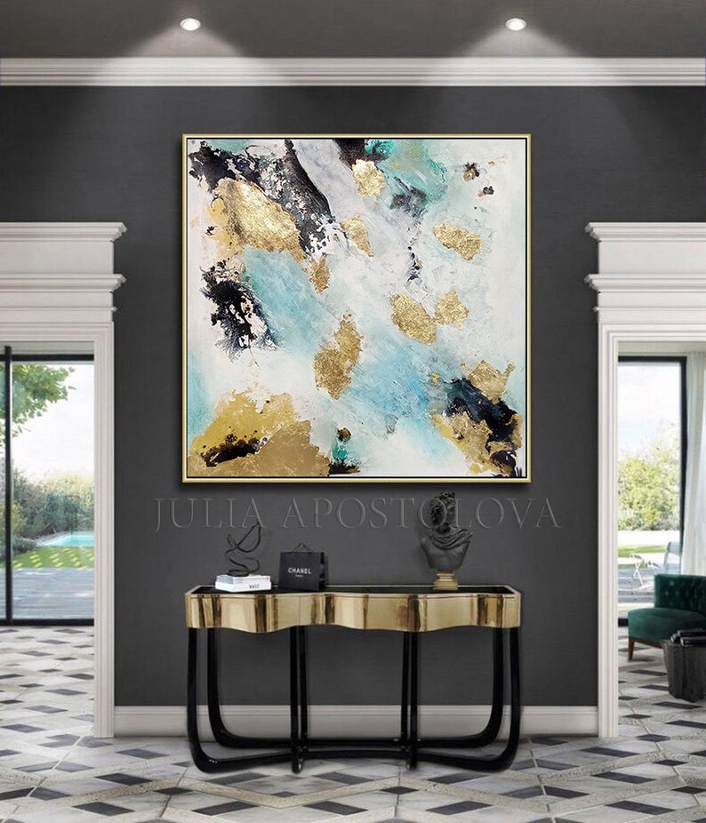 May include: Abstract painting with gold, black, and blue accents on a white background. The painting is framed in gold and hangs above a black and gold console table with a black and gold sculpture on top. The text "JULIA APOSTOLOVA" is visible below the painting.
