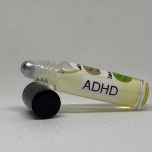 May include: A clear glass roll-on bottle with a black cap, containing a light yellow liquid. The label reads "ADHD" in bold black letters. The bottle is lying on its side.