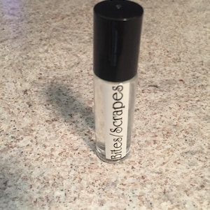 Puede incluir: Una botella de vidrio transparente con una tapa negra y una etiqueta blanca que dice "Bites/Scrapes".