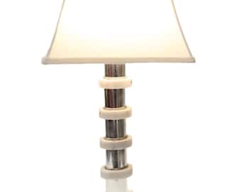 Puede incluir: Una lámpara de mesa de mármol blanco con una base plateada y una pantalla blanca. La base está formada por anillos apilados de mármol y plata.