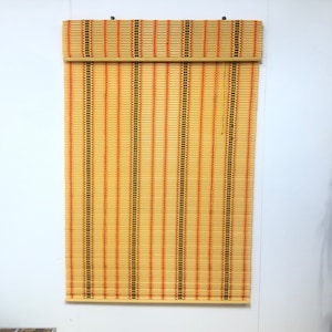 Può includere: Una tenda a rullo in bambù naturale intrecciato di colore marrone chiaro con strisce arancioni e nere.