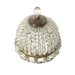 May include: A dome-shaped crystal chandelier shade featuring vertical strands of clear faceted beads hanging from a dark metal top cap. The base is encircled by a row of rectangular clear glass prisms set in a brass-toned metal frame.