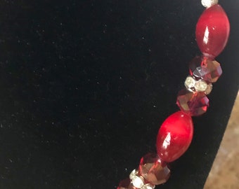 May include: A red and silver beaded necklace with oval-shaped red beads and smaller, faceted red beads interspersed with silver accents.