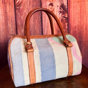 May include: A small, striped handbag with a brown leather handle and trim. The bag is made of a woven fabric with blue, white, and pink stripes.