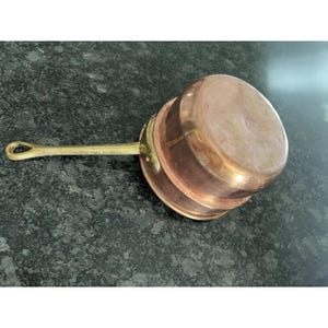 May include: A white ceramic mug with a black handle and the text "But First, Coffee" in a bold, black font. The mug is set against a blurred background, suggesting a cozy setting.