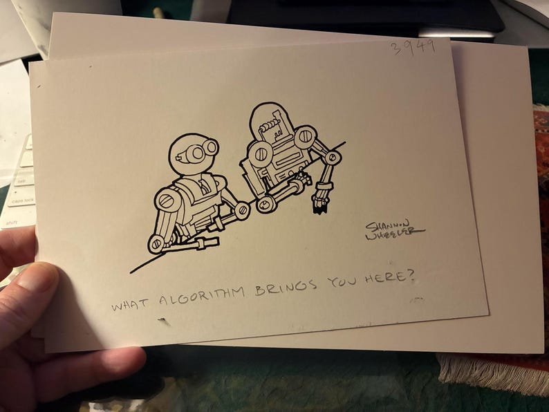 May include: A black and white ink drawing on off-white paper featuring two robots. The text reads, "WHAT ALGORITHM BRINGS YOU HERE?" and is signed "SHANNON WHEELER" with the number "3949" in the top right corner of the rectangular paper.