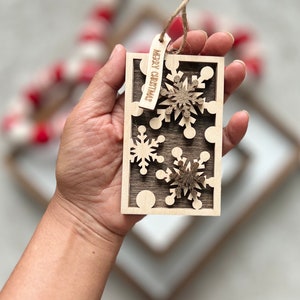 May include: A wooden Christmas ornament with a brown background and three white snowflakes. The ornament has a tag that says "Merry Christmas".