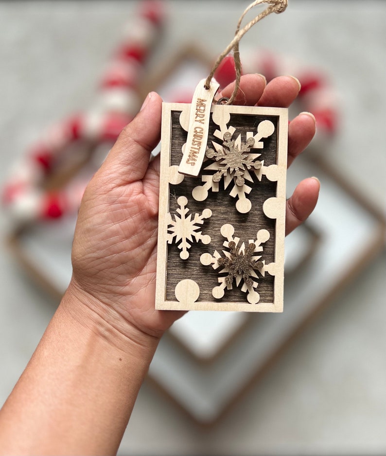 May include: A wooden Christmas ornament with a brown background and three white snowflakes. The ornament has a tag that says "Merry Christmas".