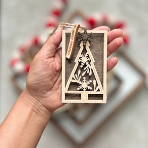 May include: A wooden Christmas tree ornament with a cutout design of snowflakes and leaves. The ornament has a brown woodgrain finish and a small tag that reads "Merry Christmas".