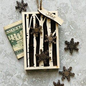 May include: A wooden Christmas ornament with a birch tree design and the name "Jake" written on a tag. The ornament is decorated with small wooden snowflakes.