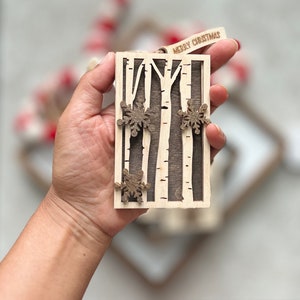 May include: A wooden Christmas ornament featuring a birch tree design with snowflakes. The ornament is brown and white and has the text "Merry Christmas" on the top.