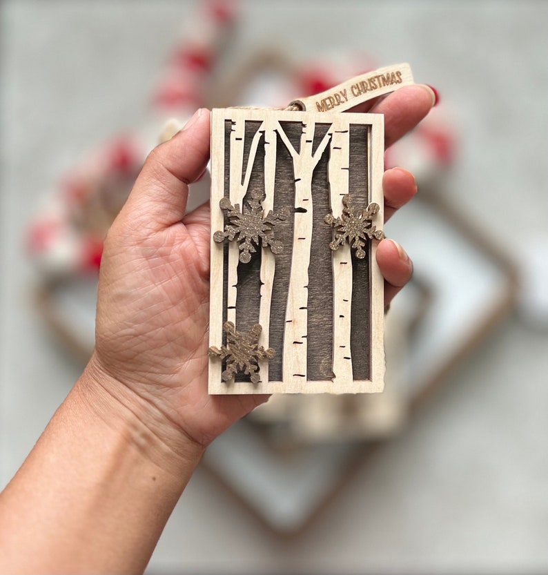 May include: A wooden Christmas ornament featuring a birch tree design with snowflakes. The ornament is brown and white and has the text "Merry Christmas" on the top.